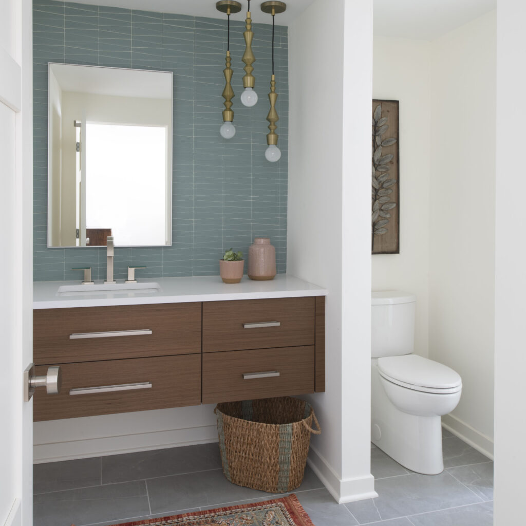Mid Century Modern Powder Room bathroom remodel, Corian Quartz, Jeffery Court backsplash, tile backsplash, teal tile, aqua tile, turquoise tile, mid-century modern vanity, modern cabinetry, lighting, frameless mirror, bathroom, primary bath, gray tile, grey tile, unique pendant lights, soft brass pendant light, antique brass pendant light, soft gold pendant lighting, wall-mounted vanity, wood vanity