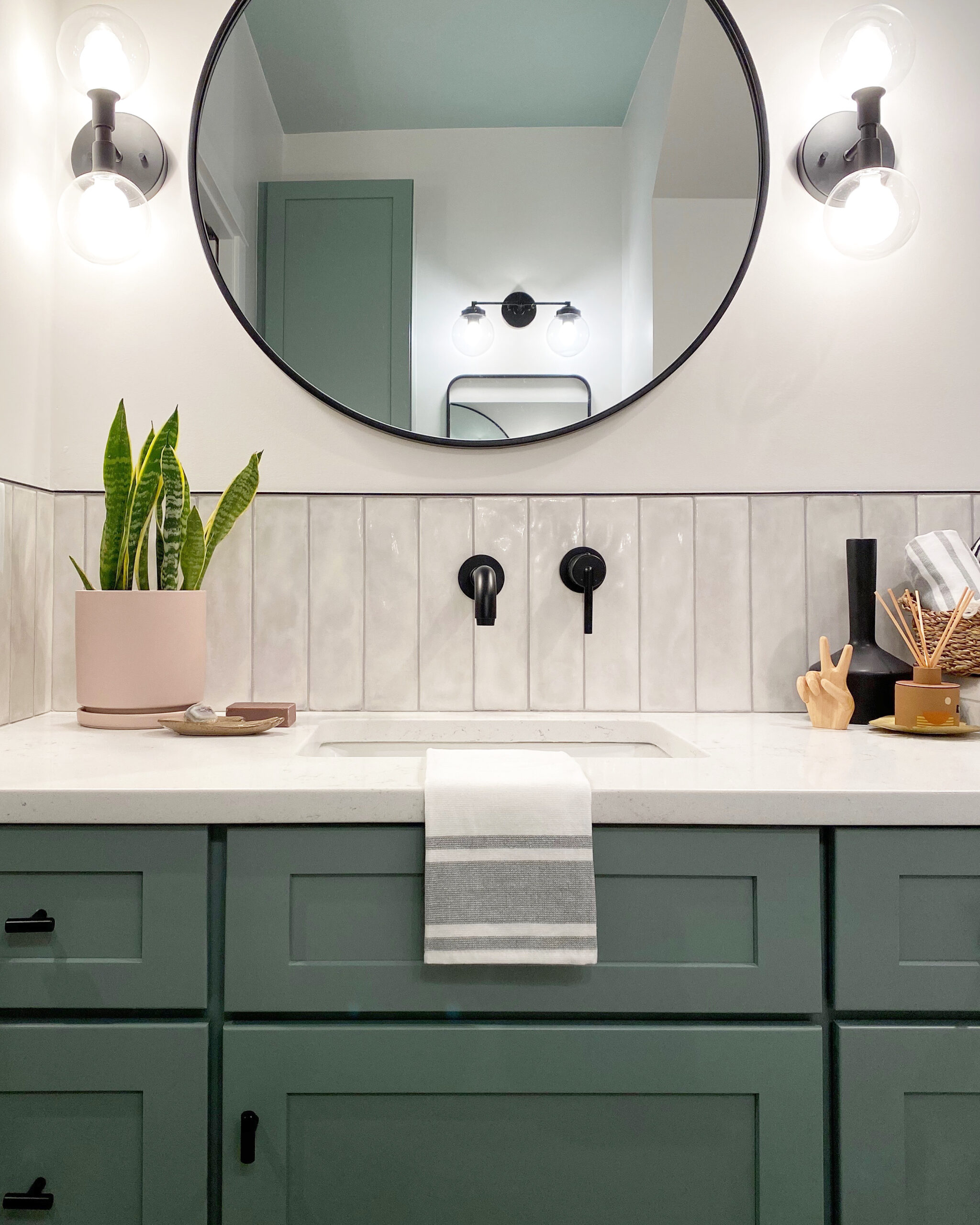 green bathroom vanity, painted cabinetry, decorative bathroom tile, vertical subway tile backsplash, round mirror